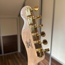 Zadní strana hlavy kytary z přírodního dřeva se zlatými ladicími kolíky. Na dřevě je černý nápis: Designed and Backed by Fender s číslem s/n IS820013…