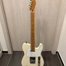 Krémová elektrická kytara typu Telecaster s javorovým hnedým hmatníkem a bílým pickguardem. Na hlavě nástroje je viditelné logo Fender. Kytara stojí…