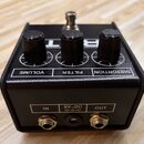 Černý efekt pedál s třemi ovládacími knoflíky a jedním zapínacím spínačem. Na horní straně jsou nápisy VOLUME, FILTER a DISTORTION. Na zadní straně j…