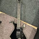 Černá elektrická kytara s ostře hranatým korpusem a bílým lemováním. Na hlavě hmatníku je viditelné logo "Jackson". Nástroj má dva humbuckery, černý…