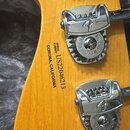 Záběr na zadní stranu dřevěné hlavy kytary s chromovanými ladičkami. Na dřevě je černý nápis SERIAL NUMBER US22046213 CORONA, CALIFORNIA. Na ladičkác…