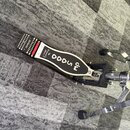 Černý bicí pedál s kovovou konstrukcí a bílou nálepkou na šlapce, na které je nápis 5000 a v menším písmu Pro Drummer. Šlapka má v horní části protis…