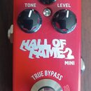 Červený efekt pedál s nápisy HALL OF FAME 2 MINI a tc electronic. Na horní straně jsou tři černé oválné ovladače s bílými popisky DECAY, TONE a LEVEL…