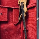 Elektrická kytara s výrazně asymetrickým, hranatým tělem z přírodního dřeva v hnědém odstínu. Nástroj má dva černé humbuckery, tři ovládací knoflíky…