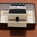 Bílý efekt pedál s nápisy Digital Delay a DD-7. Na horní části jsou modré konektory s popisky OUTPUT B, OUTPUT A, INPUT B (STEREO) a INPUT A (MONO),…