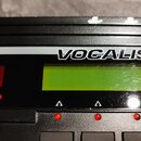 Detailní záběr na ovládací panel černého elektronického zařízení. Je zde vidět bílý pruh s nápisy VOCALIST VHM5 a fragmentem slova ech. Panel obsahuj…