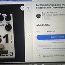 Bílý efekt pedál s černými ovládacími knoflíky. Na horní části je nápis AMT a popisky LOW, MID, HIGH, LEVEL a GAIN. Ve spodní části je velký nápis S1…