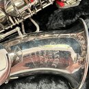 Detail stříbrného saxofonu v černém polstrování. Na čáře nástroje je vyryt nápis CLASSIC SUPER, pod ním slova "Smooth" a "asglice", dále text MADE IN…