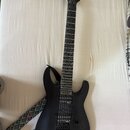 Černá elektrická kytara s matným povrchem a šesti strunami. Na hlavě hmatníku je bílý nápis Jackson. Nástroj má dva humbuckery, jeden ovládací knoflí…
