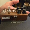 Hnědý efekt pedál s kovovým povrchem a čtyřmi černými ovládacími knoflíky. Na horní straně je nápis bass fuzz deluxe a logo MXR BASS INNOVATIONS. Na…