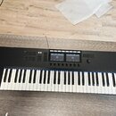 Černý MIDI kontrolér s klávesnicí. Na levé straně je bílý nápis KOMPLETE s logem vedle. Horní panel obsahuje několik sad tlačítek, dva displeje a jed…