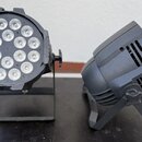 Dvě černé LED osvětlovací jednotky na stojáncích. Levý reflektor má kulatý tvar s 12 viditelnými LED diodami v mřížce. Pravý reflektor má kompaktnějš…