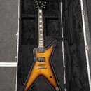 Elektrická kytara s pěticípým tělem v barevném přechodu od žluté k černé, umístěná v černém tvrdém kufru. Nástroj má dva humbuckery, stříbrný most a…