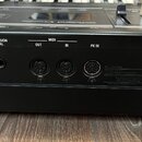 Záběr na zadní panel černého klavírního nástroje. Jsou zde viditelné konektory s nápisy DAMPER, EXPRESSION PEDAL, MIDI OUT, MIDI IN, PK IN a EXT INPU…