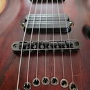 Detail elektrické kytary s tmavě červeným dřevěným povrchem. Na fotce je vidět černý humbucker, černý kobylník a šest kovových kotvic pro struny. Pov…