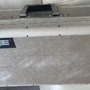 Stříbrný transportní kufr s kovovými hranami, rohy a dvěma zapínacími zámky. Na přední straně je černý obdélníkový štítek s modrobílým nápisem SHURE.…