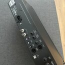 Zadní strana černého elektronického zařízení s řadou konektorů a ovládacích prvků. Jsou zde nápisy INPUT, MIDI IN/OUT THRU, FOOT Input, Output Balanc…