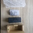 Na fotografii je černý efekt pedál s vlnovitým reliéfem na povrchu a nápisem BOSS. Vedle něj se nachází papírová dokumentace v plastovém obalu, průhl…