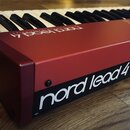 Červený syntetizátor s klávesnicí. Na boku je bílý nápis „nord lead 4“ a v levém dolním rohu menší označení „v2.5“. Povrch nástroje je hladký a v dob…