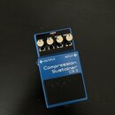 Modrý efekt pedál s nápisy Compression Sustainer a CS-3. Na horní části jsou čtyři bílé ovládací knoflíky s popisky LEVEL, TONE, ATTACK a SUSTAIN, če…