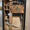 Fotografie zachycuje vnitřek černého dřevěného rámu s elektronickými komponenty. Uvnitř je umístěna základní deska s plošnými spoji, pájenými kontakt…