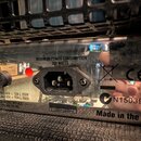 Detail zadní strany zařízení s kovovým, reflexním povrchem. Je zde viditelný napájecí konektor a nápisy: „MAXIMUM POWER CONSUMPTION 300 WATTS“, „SUPP…
