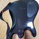 Zadní strana elektrické kytary v černé barvě s lesklým povrchem. Na těle je vidět krycí plastový kryt elektroniky a čtyři šrouby u základny krku. Pov…