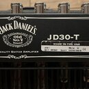 Detailní pohled na horní panel černého kytarového zesilovače s pěti kovovými oválnými knoflíky. Na panelu je bílý nápis JACK DANIEL'S, logo Old No.7…