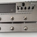 Stříbrný efektový procesor s kovovým povrchem a displejem. Na horním panelu je nápis GE3CC Amp modeling & Multi effects, dále označení EXP1, EXP2, XL…