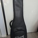 Černý polotvrdý pouzdro (gig bag) na kytaru z materiálu s texturou kůže. V dolní části je bílý nápis Gibson. Pouzdro má připevněné úchytné madlo a zi…