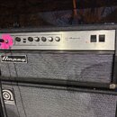 Černý basový zesilovač značky Ampeg umístěný na basovém reproduktoru stejné značky. Na horním ovládacím panelu jsou nápisy gain, ultra lo, bass, midr…