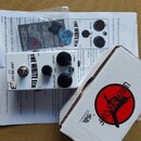 Bílý efekt pedál s nápisy THE WHITE ELK, UREN AND CUFF a USA. Na horní straně jsou tři černé ovládací knoflíky s popisky VOLUME, TONE a DISTORTION. P…