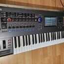 Černý digitální syntezátor s klávesnicí. Na levé straně horního panelu je logo a nápis YAMAHA, na pravé straně nápis MONTAGE. Přístroj obsahuje numer…