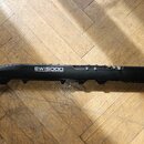 Černý elektronický dechový nástroj s nápisy EWIS5000 WIRELESS ELECTRONIC WIND INSTRUMENT a AKAI PROFESSIONAL. Nástroj leží na dřevěné podlaze. Povrch…
