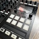 Detailní pohled na ovládací panel černého DJ kontroléru. Jsou vidět bílé podsvícené čtvercové pady s popisky HOTCUE, FREEZE, REMIX a FLUX, dále tlačí…