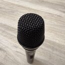 Černý dynamický mikrofon s kovovou mřížkou. Na těle je viditelné bílé logo značky AKG. Povrch mikrofonu vykazuje mírné známky opotřebení v podobě dro…