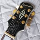 Detail hlavy černé elektrické kytary s bílým lemováním a zlatými ladičkami. Na horní části je bílé logo Epiphone a v dolní části nápis Les Paul CUSTO…