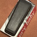 Černý wah-wah pedál s žebrovaným povrchem šlapadla, umístěný v originální červeno-bílé krabici. Na boku krabice je bílý nápis cry baby. Na šlapadle j…
