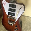 Elektrická kytara s hnědým dřevěným korpusem a bílým pickguardem. Nástroj má tři černé humbuckery, chromovaný most a bílý pákový mechanismus. Na horn…
