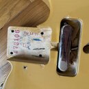 Detail zadní strany krku žluté kytary s viditelným spojem u těla. Na dřevěném bloku je červeným inkoustem napsáno #73106 a JUL 05 201, dále jsou zde…