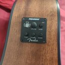 Detail ovládacího panelu akustické kytary s dřevěným povrchem. Černý plastový panel nese nápisy FISHMAN®, volume, tuner, batt, bass, middle a treble,…