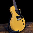 Žlutá elektrická kytara s celobody a černým pickguardem umístěná na černém stojanu. Nástroj má dva humbuckery, jeden Tune-o-matic můstek a dva ovláda…