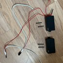 Dvě černé hranaté elektroniky s logem emg, pravděpodobně aktivní snímače. K nim patří červené a bílé vodiče s konektory a jeden černý kabel zakončený…
