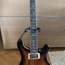 Polodublová elektrická kytara s tmavě hnědým gradientem (sunburst) a dvěma humbuckery. Na hlavě je bílý nápis "Cort" a menší text "Piezo". Hmatník ob…