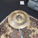 Zlatý kovový činel namontovaný na stojanu. Na povrchu je viditelný nápis Istanbul Agop Handmade Cymbals Turkey B20. Činel vykazuje známky používání v…