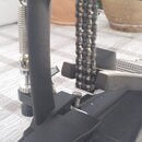 Detailní záběr na černý kovový mechanismus s řetězem. Zařízení obsahuje pružinu, nastavovací šrouby a plastové dopinky. Na komponentech nejsou žádné…
