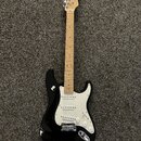 Černá elektrická kytara s bílým pickguardem a světlou dřevěnou hmatnicí. Na hlavě je viditelné logo Fender. Nástroj má tři snímače typu single-coil,…