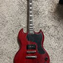 Červená elektrická kytara s černým pickguardem a hnedým hmatníkem. Na hlavě je viditelné logo Epiphone. Tělo vykazuje drobné známky opotřebení a povr…