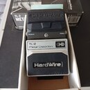 Kytarový efekt v šedém kovovém krytu, umístěný v bílém kartonovém obalu před originální krabicí. Na pedálu je nápis TL-2 Metal Distortion a logo Hard…