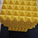 Zásobník žlutých akustických absorbů z pěny s pyramidovitým povrchem. Panely jsou naskládány na sebe v několika vrstvách. Na fotografiích nejsou vidi…